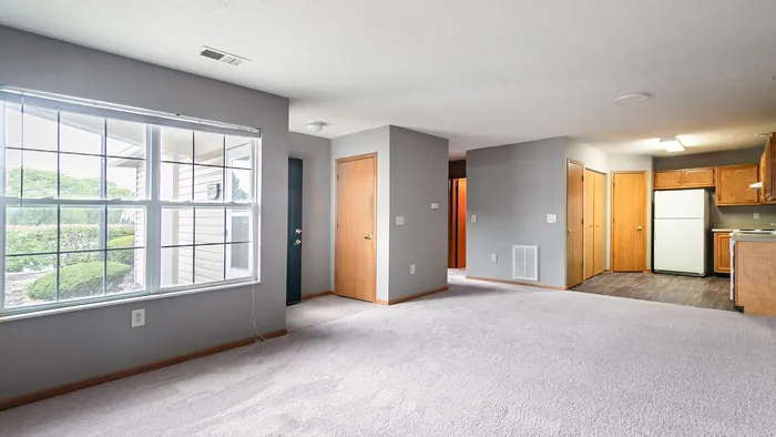 Bright and inviting apartment interior featuring plush carpeted flooring, expansive windows for abundant natural light, and a modern kitchen with sleek appliances.