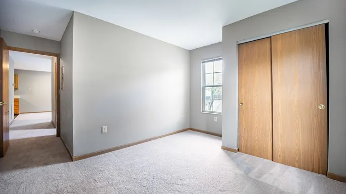 Bright and spacious room featuring soft carpeting, a large sunny window, and cozy wooden closet doors.