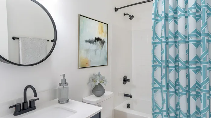 Modern bathroom with elegant black fixtures, stylish round mirror, and artistic decor. Features a spacious shower with a chic blue-patterned curtain.