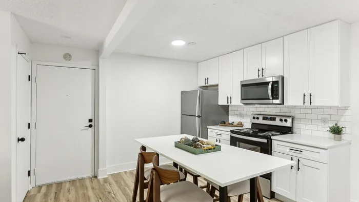 Modern kitchen with sleek white cabinetry, stainless steel appliances, and a chic dining table set on elegant wood flooring.