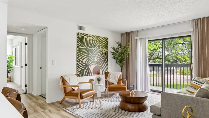 Bright, modern living room with elegant decor, featuring lush greenery, stylish leather chairs, and a view of the outdoors through sliding glass doors.