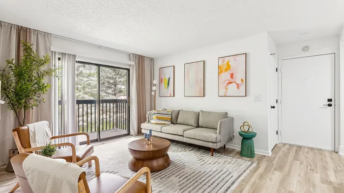 Bright and inviting living room with elegant modern decor, featuring a comfortable sofa, stylish armchairs, and large sliding glass doors opening to a scenic balcony view.