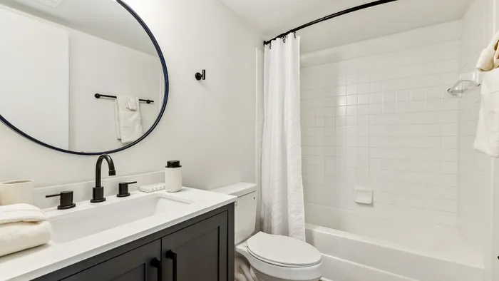 Elegant bathroom featuring a sleek vanity with a modern matte black faucet, large circular mirror, and a pristine white bathtub with a stylish shower curtain.