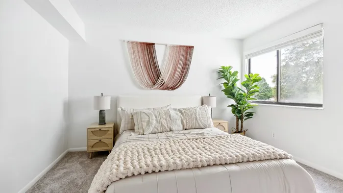 Bright and airy bedroom with a cozy bed, elegant wall art, and a lush potted plant by the window.
