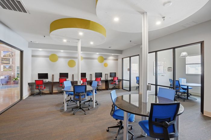 Modern shared workspace with vibrant seating, computer stations, and glass-enclosed meeting rooms, designed for productivity and collaboration.