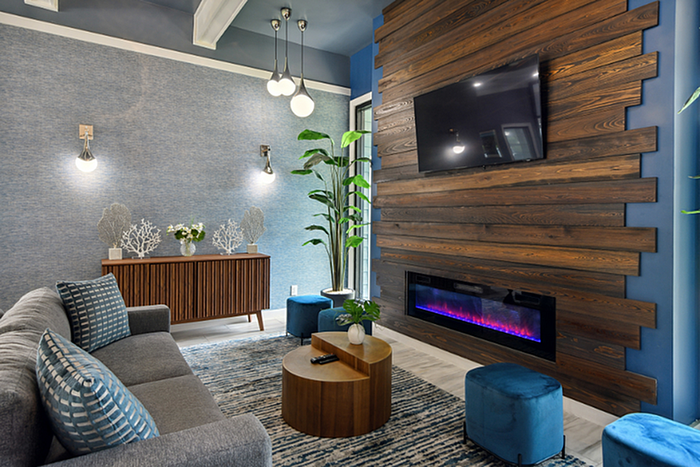 Modern living room with chic gray sofa, wooden accent wall, electric fireplace, and elegant lighting, offering a cozy and stylish ambiance.