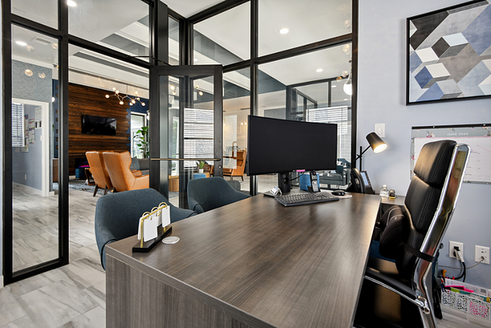 Modern office space featuring sleek glass walls, stylish desk, and contemporary lounge area with vibrant seating.