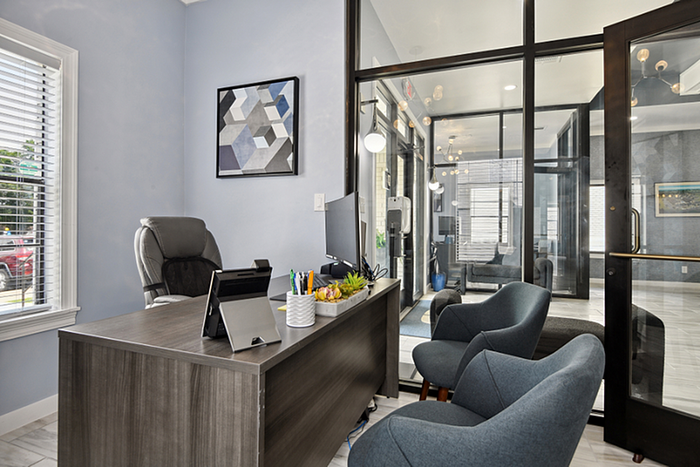 Modern office space with large glass windows, stylish furniture, and ample natural light, creating a welcoming and productive environment.