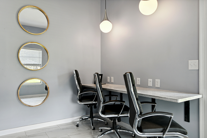Modern workspace with sleek chairs and a long desk, enhanced by circular mirrors and elegant lighting.