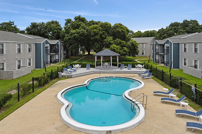 Inviting outdoor pool area with stylish lounge chairs and a charming gazebo, nestled between modern apartment buildings surrounded by lush greenery.
