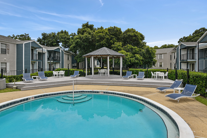 Elegant apartment complex with inviting pool area, modern lounge chairs, and shaded gazebo, surrounded by lush greenery.