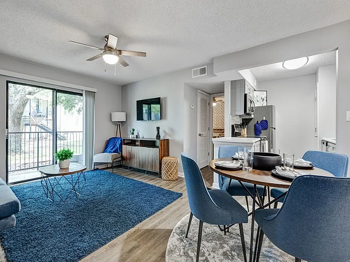 Bright open living area featuring a modern dining set, cozy seating, and stylish decor with a view of the lush outdoors through sliding glass doors.