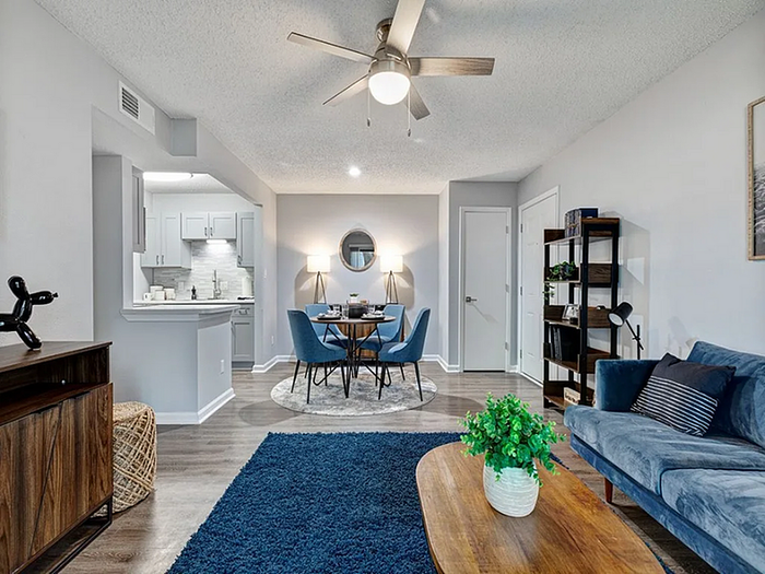 Chic open-plan living space featuring a cozy blue sofa, elegant dining area, and modern kitchen with sleek cabinetry.