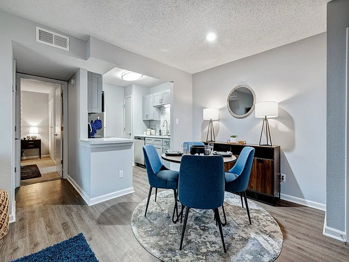 Chic open-concept dining area with stylish blue chairs, elegant lighting, and a cozy modern kitchen.