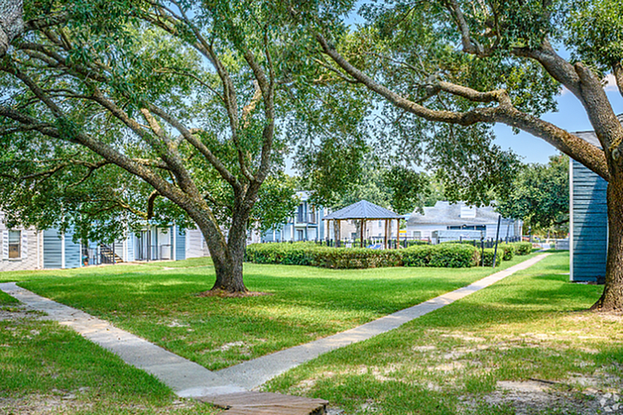 Serene apartment complex setting with lush green lawns, mature trees, and charming gazebo.