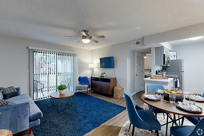 Modern open living room with plush blue seating, sleek dining area, and stylish kitchen, flooded with natural light.