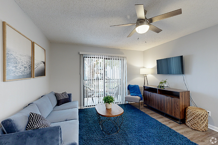 Inviting living room with modern decor, plush blue carpet, and sliding glass doors opening to a serene outdoor view.