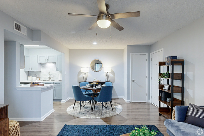 Modern open-concept living and dining area with stylish furnishings, featuring a cozy blue theme and a sleek ceiling fan.