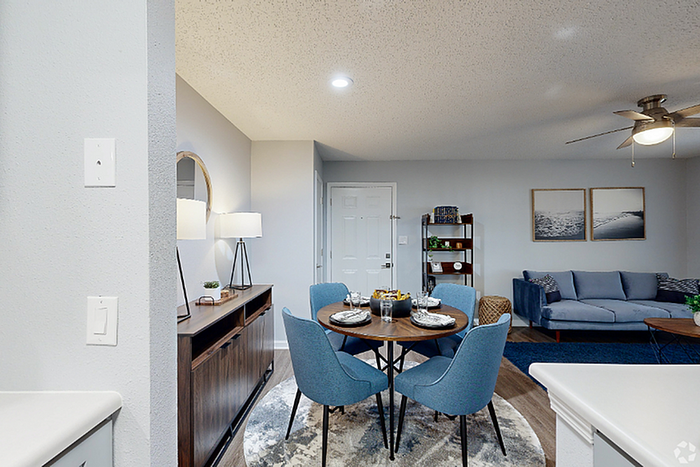 Modern apartment interior showcasing a cozy seating area, elegant dining set with blue chairs, and stylish decor in a well-lit living space.