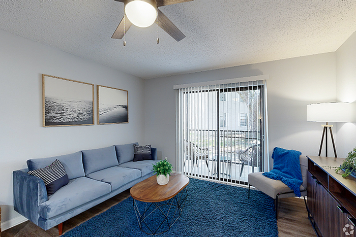 Inviting living room with cozy blue sofa, stylish coffee table, modern ceiling fan, and bright natural light from large patio doors.