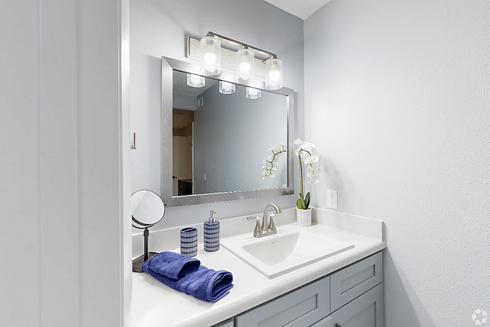 Elegant bathroom with a sleek countertop, stylish mirror, and modern light fixtures, complemented by chic blue accessories and a delicate orchid decoration.