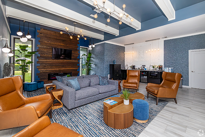 Modern apartment lounge with sleek blue and wood accents, featuring cozy seating, stylish lighting, and ample natural light.