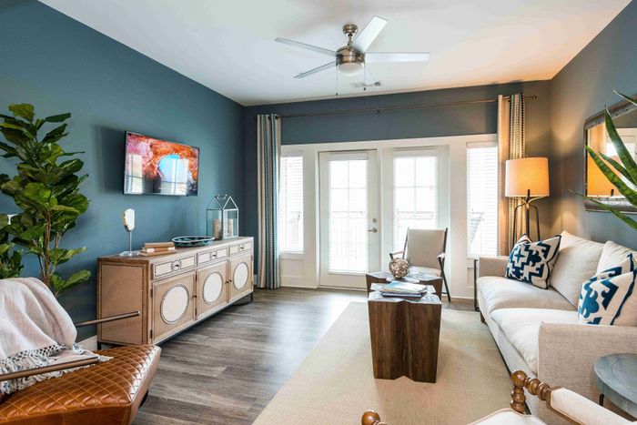 Living room with a blue accent wall, sofa, television and balcony doors.