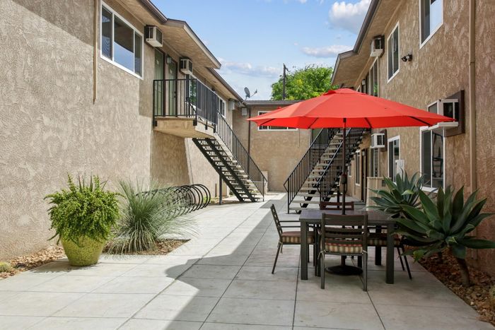 Charming apartment courtyard with modern outdoor seating under a vibrant red umbrella, surrounded by lush greenery and elegant staircases.