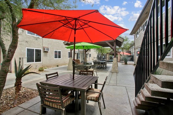 Charming outdoor patio with vibrant red and green umbrellas, featuring stylish seating in a serene apartment courtyard.