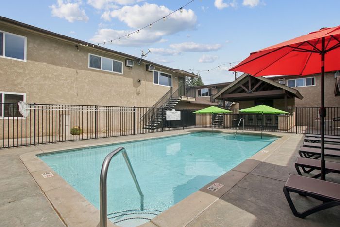 Inviting outdoor pool area with modern lounge chairs, vibrant umbrellas, and surrounding apartments, perfect for relaxation and social gatherings.
