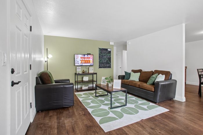Inviting living room with a modern leather sofa, cozy armchair, stylish decor, and wall-mounted TV against a soothing green accent wall.