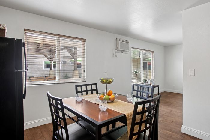 Bright dining area with a modern table set, wood flooring, and airy windows overlooking a peaceful patio.