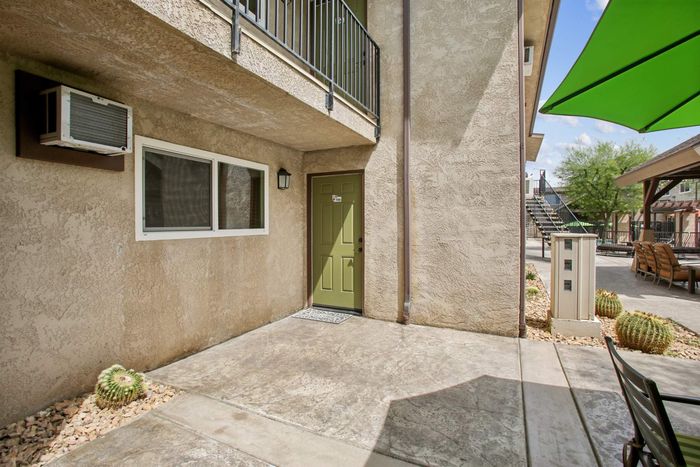Inviting apartment entrance with a green door and charming outdoor seating area, surrounded by desert landscaping and stylish architecture.