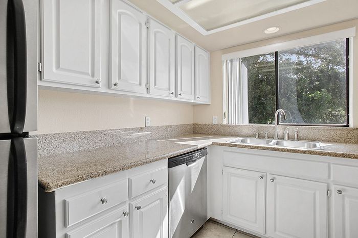 Bright modern kitchen with white cabinets, granite countertops, stainless steel appliances, and a large window inviting natural light.