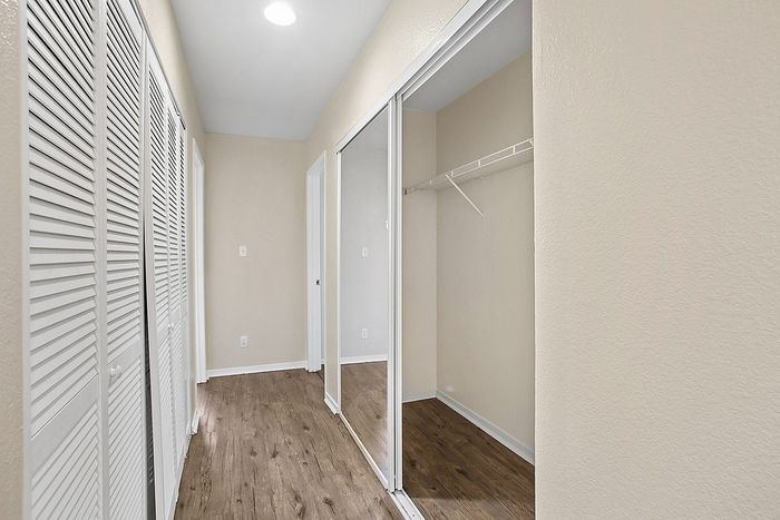 Bright hallway with elegant hardwood flooring, featuring spacious closets and modern lighting.