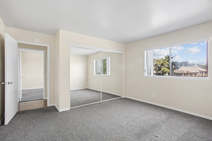 Bright bedroom with large mirrored closet and a scenic window view, offering ample natural light and fresh ambiance.