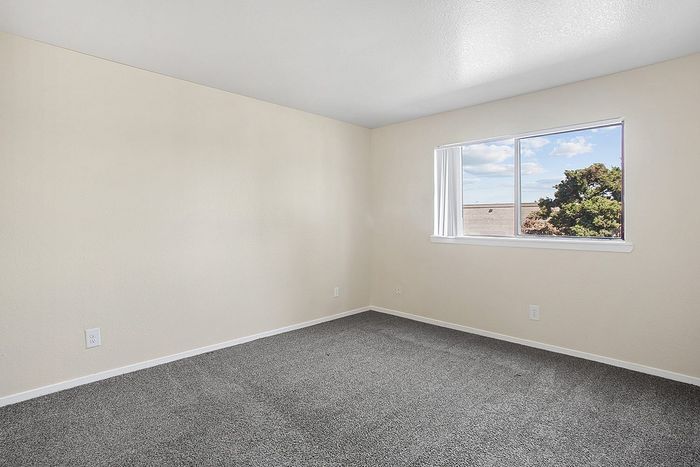 Bright and inviting bedroom with soft carpet flooring and a large window offering natural light and scenic views.