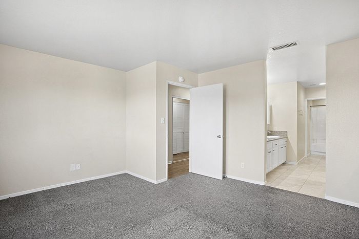 Bright and freshly updated apartment room with soft carpet flooring, leading to a sleek bathroom featuring elegant tiling and a modern vanity.
