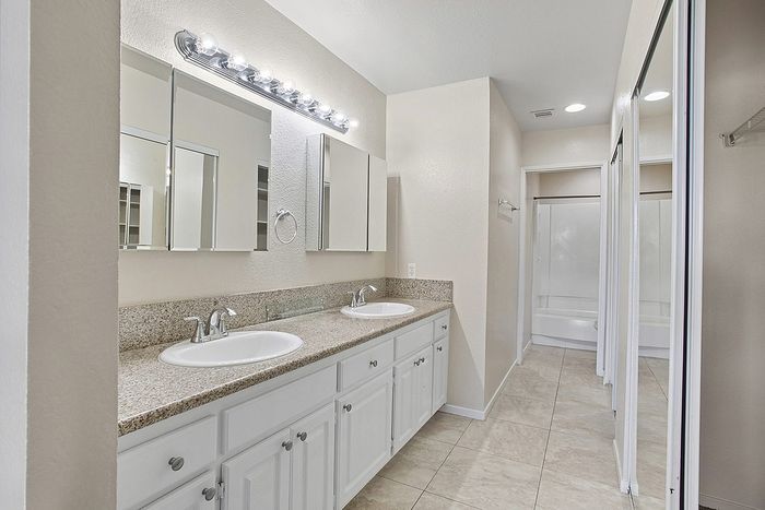 Elegant bathroom with dual sinks, granite countertops, and ample storage space, enhanced by bright lighting and modern fixtures.
