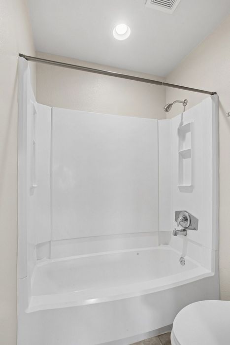 Modern white bathroom with a sleek bathtub and shower combination, illuminated by recessed ceiling lighting.