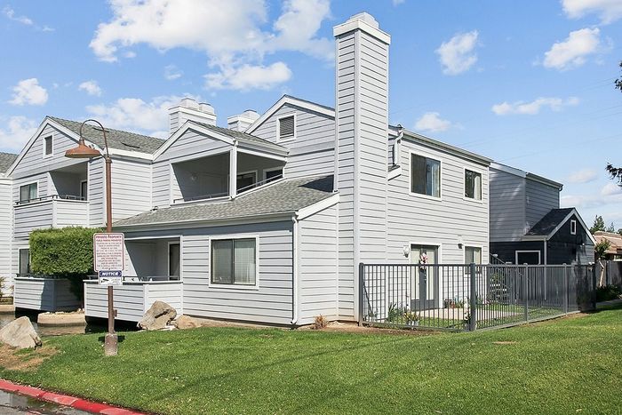 Charming two-story apartment building with modern design, private balconies, and a lush green lawn.