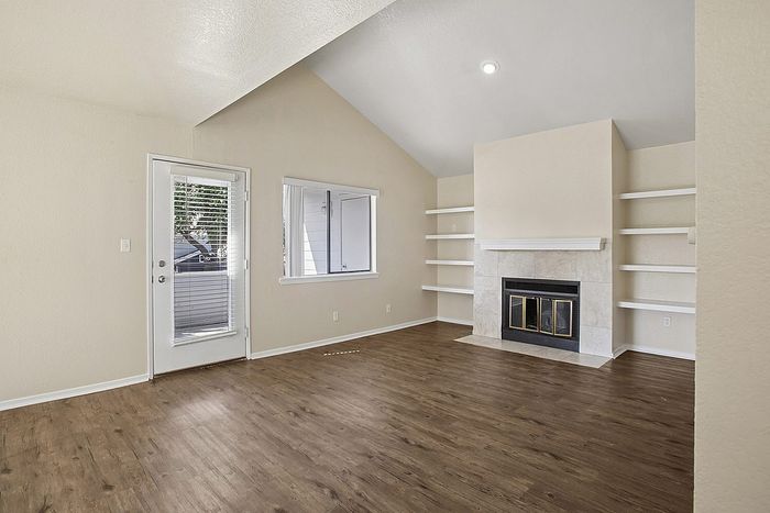 Bright living room with vaulted ceilings, cozy fireplace, and elegant shelving in a modern apartment.