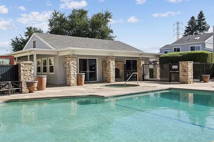 Charming residential property with a refreshing swimming pool under a clear blue sky, featuring elegant stone columns and lush greenery.