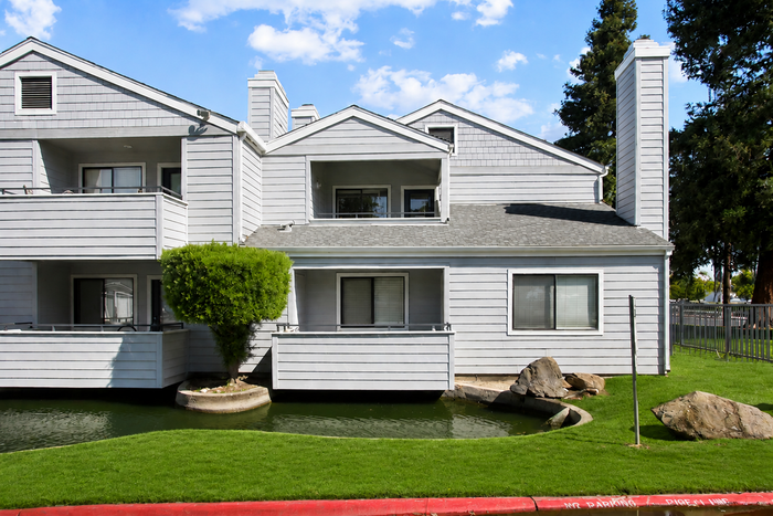 Charming townhouse with modern grey exterior and lush landscaping, featuring spacious balconies and scenic pond views.