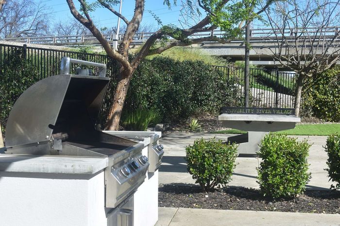Inviting outdoor space with a modern barbecue grill and lush greenery at University River Village.