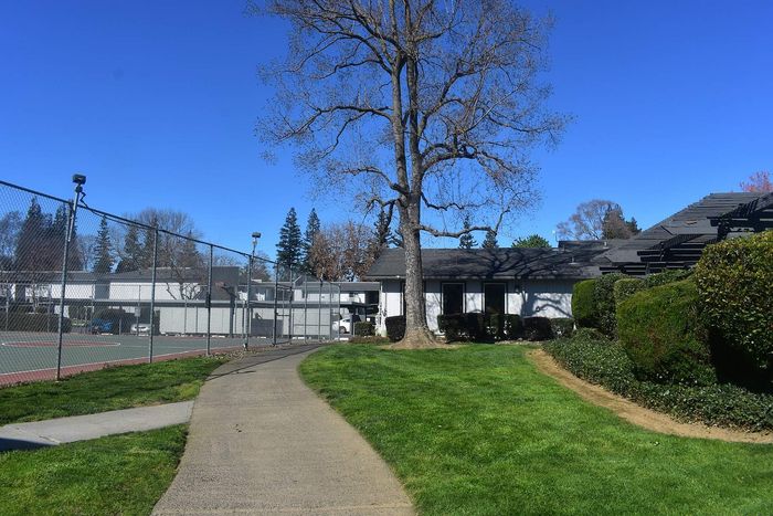 Sunny apartment complex with lush green landscaping, adjacent to tennis courts, perfect for active living.