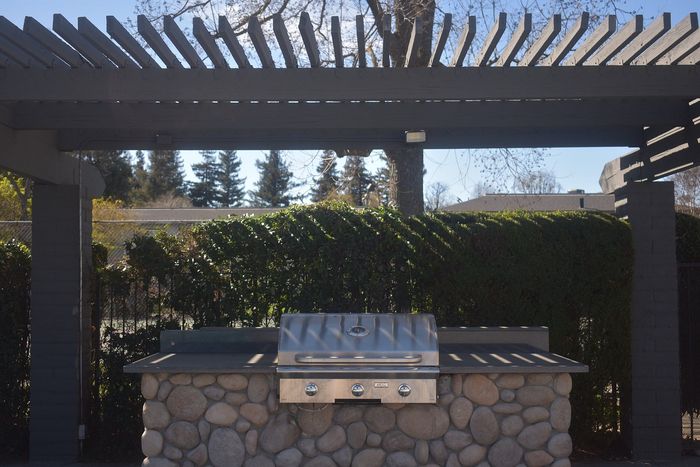 Charming outdoor barbecue area with a sleek stone countertop and a modern grill beneath a stylish wooden pergola, perfect for outdoor entertaining.