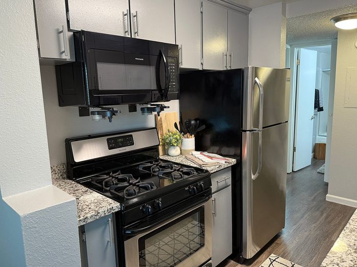 Modern kitchen featuring stainless steel appliances, sleek cabinetry, and elegant granite countertops, leading to a well-lit hallway.