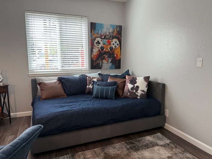 Cozy living area featuring a stylish gray daybed with accent pillows, vibrant artwork, and ample natural light from the window.