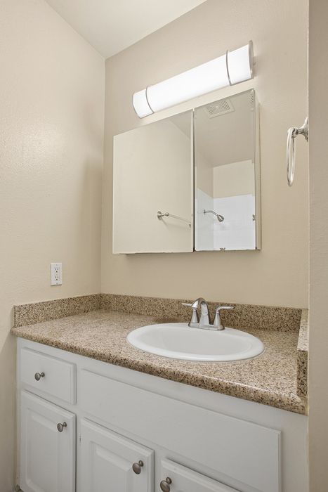 Bright and modern bathroom featuring a sleek granite countertop, elegant mirror, and stylish vanity lighting.